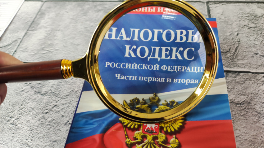 Налоговый кодекс под лупой на фоне серого стола