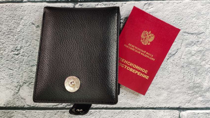 Пенсионное удостоверение рядом с кожаным портмоне на светлом фоне