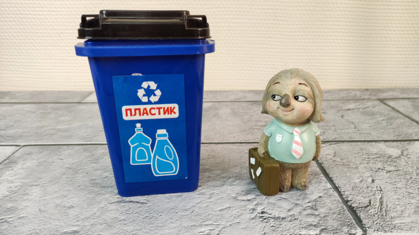 Фигурка ленивца рядом с контейнером для пластика