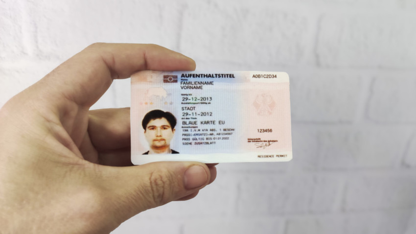 Немецкий вид на жительство Blue Card EU в руке на фоне стены