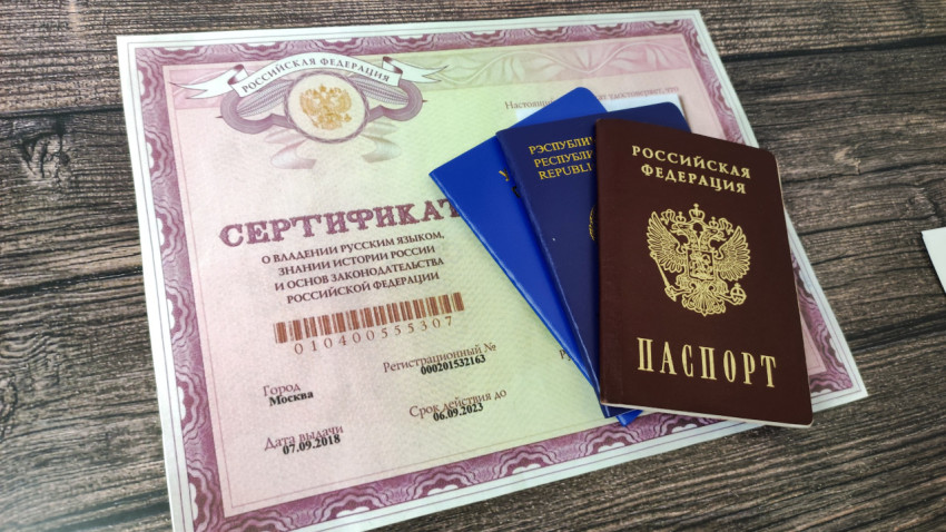 Паспорта России, Украины и Беларуси на деревянном столе, рядом с сертификатом о знании русского языка