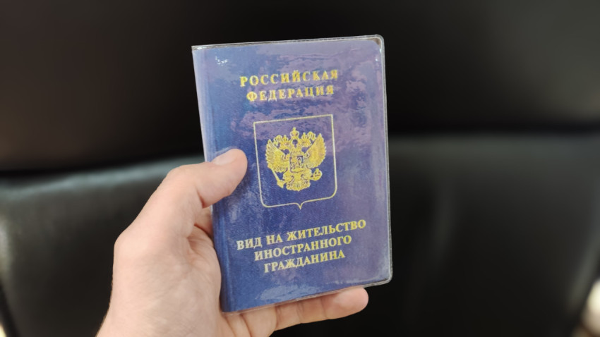 Вид на жительство иностранного гражданина в руке на фоне чёрного кресла
