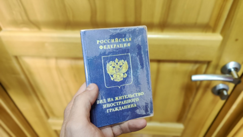 Вид на жительство иностранного гражданина в руке на фоне деревянной двери