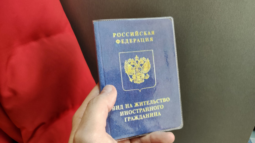 Вид на жительство иностранного гражданина в руке на фоне красной ткани