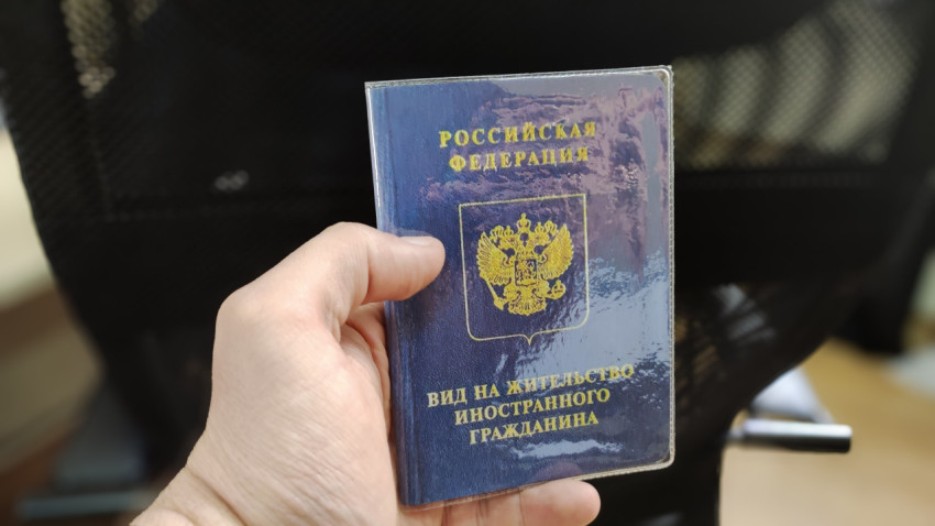 Вид на жительство иностранного гражданина в руке на фоне офисного кресла