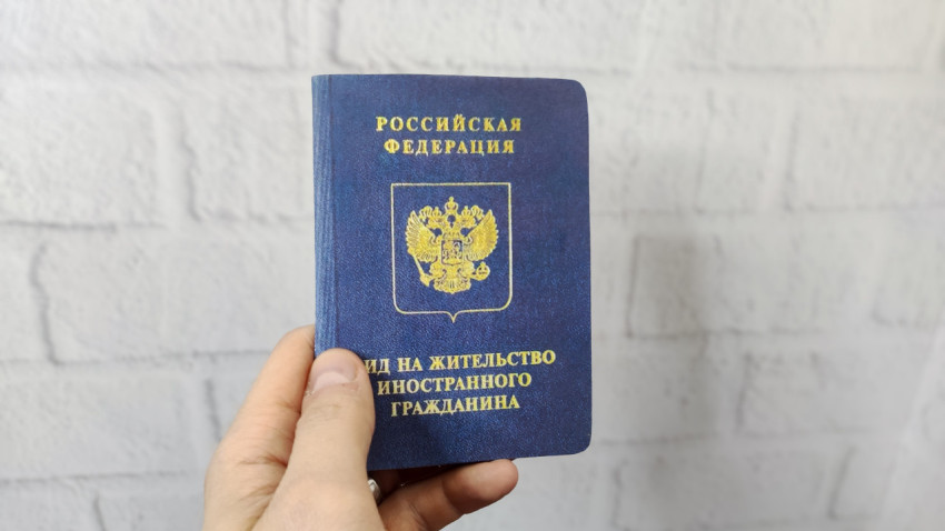 Вид на жительство иностранного гражданина Российской Федерации в руке на фоне белой стены