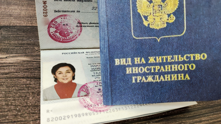 Вид на жительство иностранного гражданина в обложке и паспорт РФ на деревянном столе