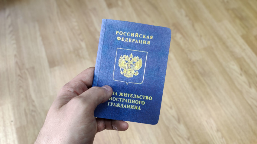 Вид на жительство иностранного гражданина в руках на фоне деревянного пола