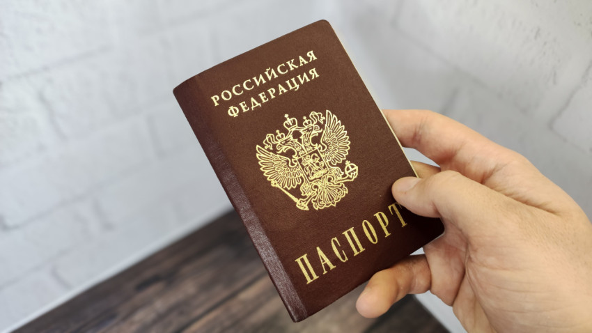 Паспорт Российской Федерации в правой руке на фоне стены