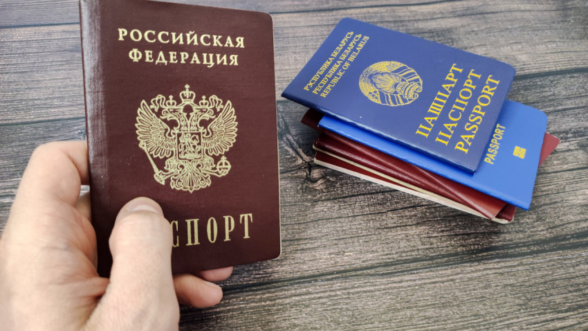 Паспорт России в руке и белорусский паспорт в стопке других паспортов на фоне