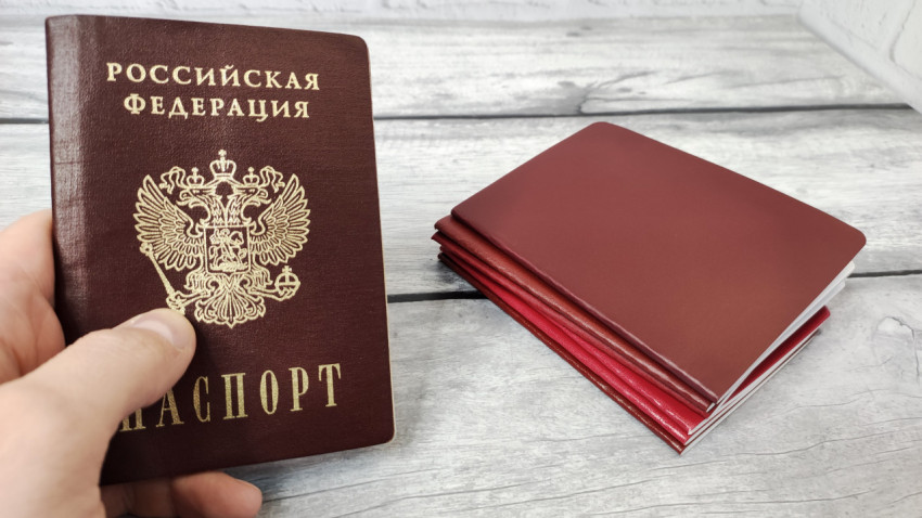 Паспорт Российской Федерации в руке и стопка бордовых обложек