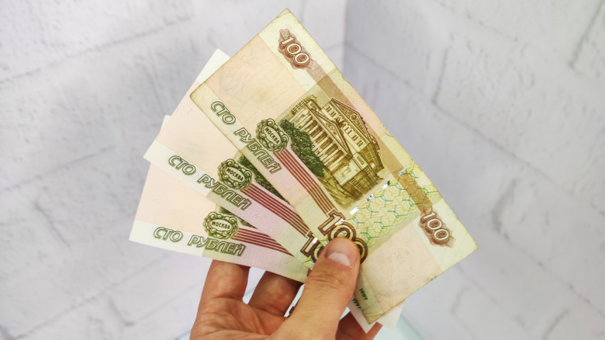Три банкноты по 100 рублей в руке