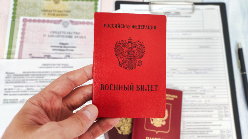 Военный билет России в руке на фоне документов и паспорта