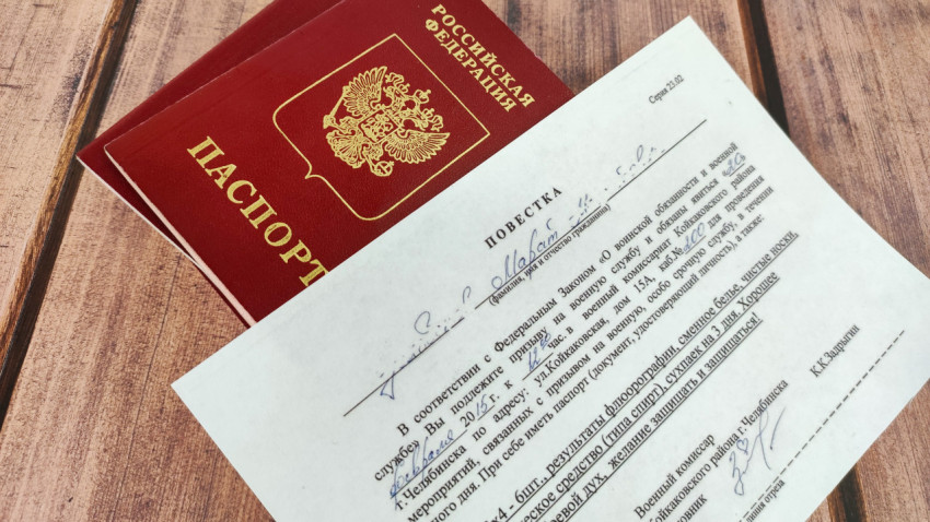 Заграничный паспорт и повестка в военкомат на деревянном фоне