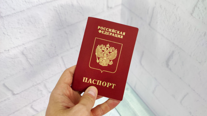 Заграничный паспорт Российской Федерации в руке на фоне светлой стены