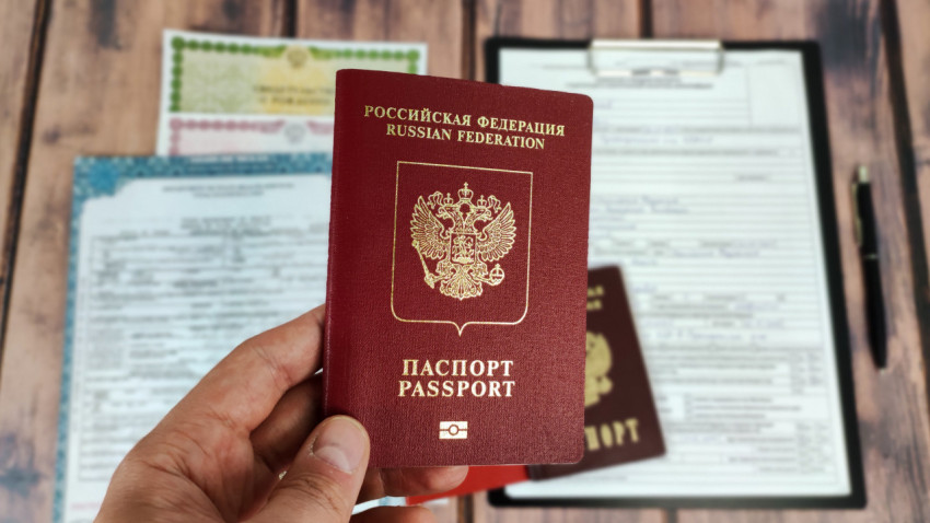 Российский загранпаспорт в руке на фоне свидетельства о смерти