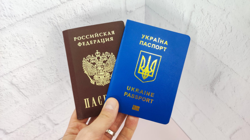 Российский и украинский паспорта в руке на фоне стены