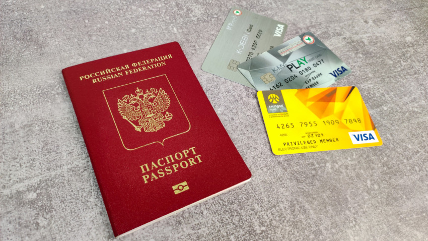Загранпаспорт Российской Федерации и тайские банковские карты на серой поверхности