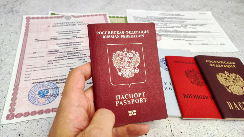 Загранпаспорт в руке на фоне свидетельства о браке и других документов