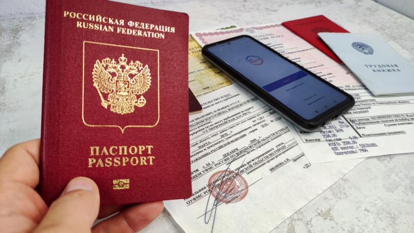 Загранпаспорт РФ в руке на фоне документов и смартфона с Госуслугами