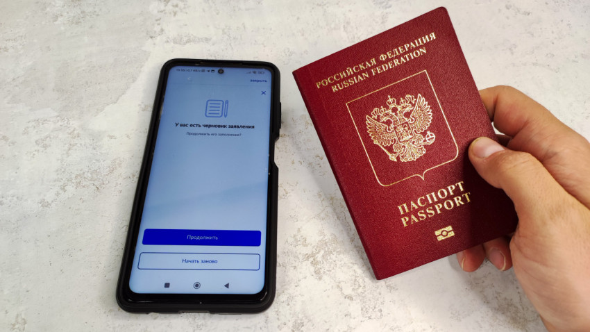Загранпаспорт России в руке и смартфон с приложением Госуслуги