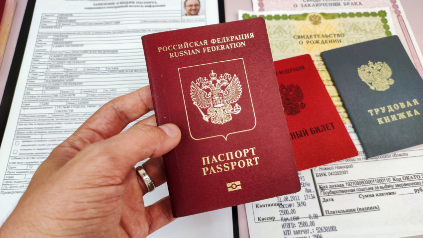 Заграничный паспорт РФ в руке на фоне заявления и документов