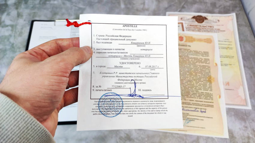 Апостиль в руке над доверенностью и свидетельством