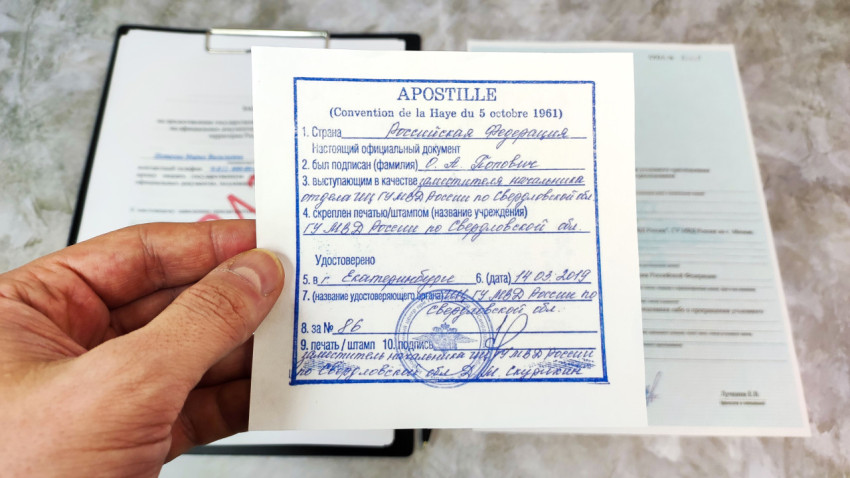 Апостиль Российской Федерации в руке над заявлением и справкой МВД