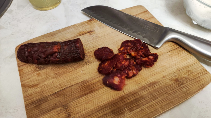 Нарезка колбасы на деревянной доске с ножом