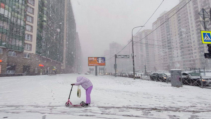 Пешеход с самокатом в пурге у многоэтажных домов