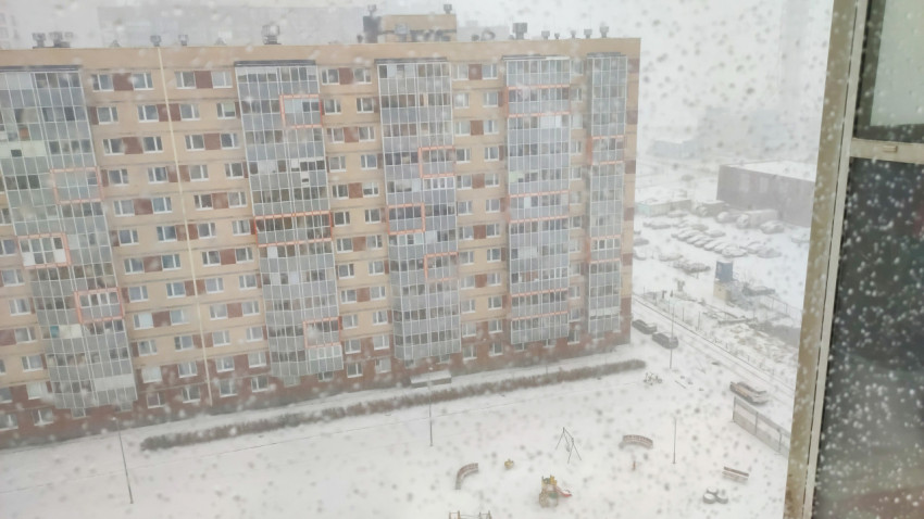 Вид на жилой дом и двор через окно во время снегопада