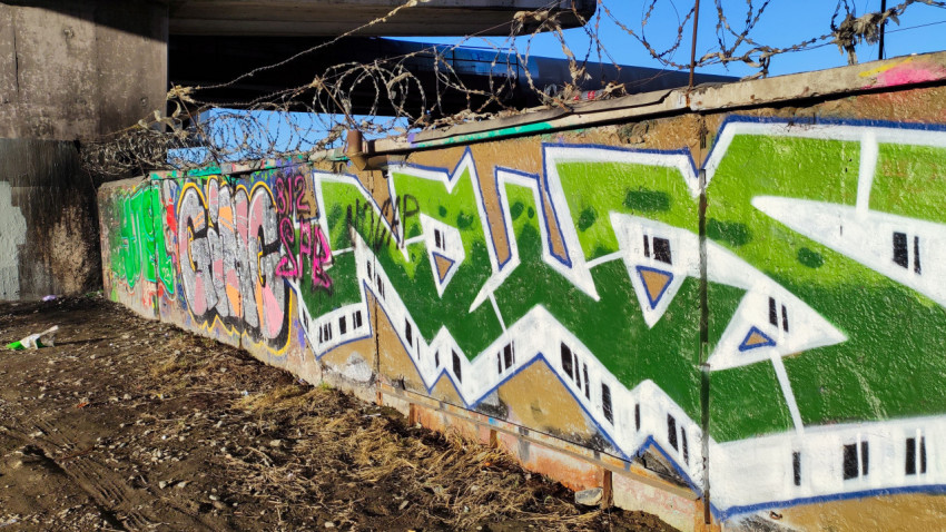 Граффити на бетонной стене под мостом с колючей проволокой