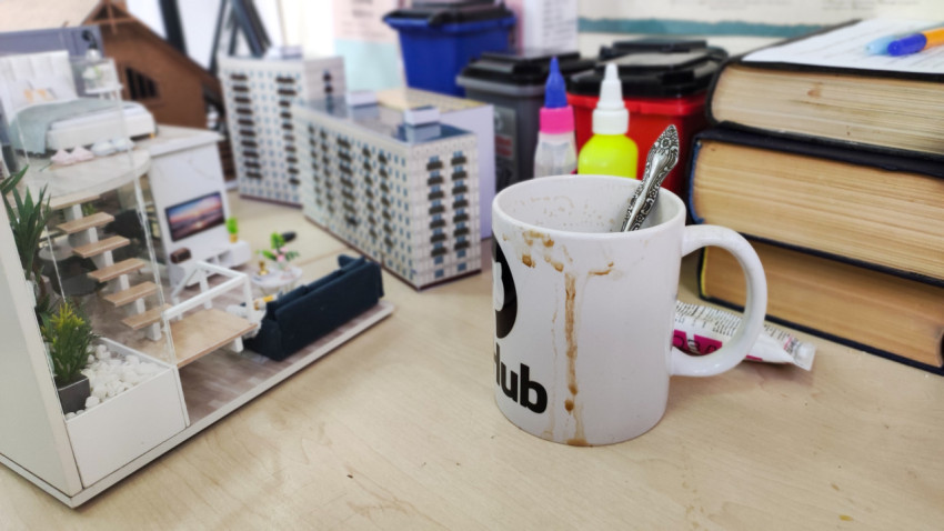 Рабочий стол с миниатюрными макетами домов и используемой кружкой