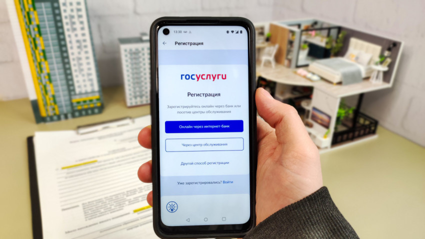Смартфон с экраном регистрации в приложении «Госуслуги» на фоне макетов домов и интерьера