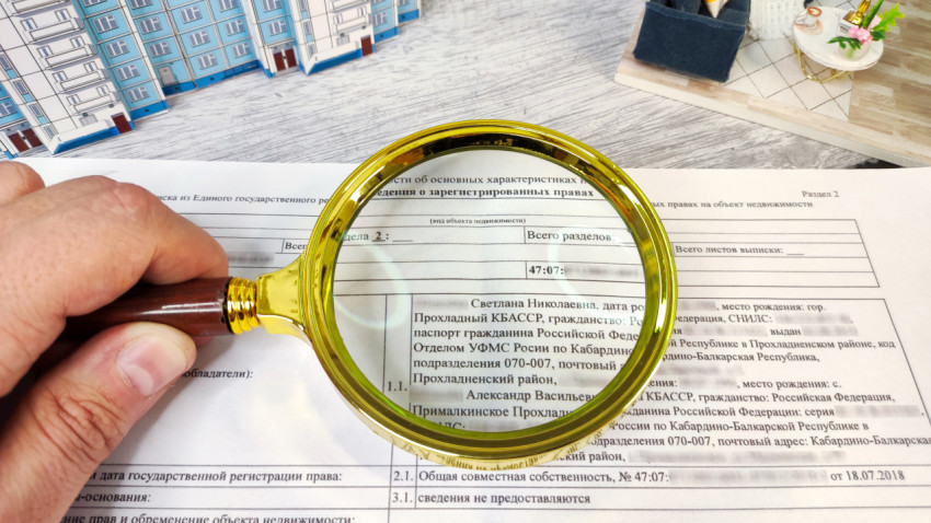 Лупа над документом ЕГРН на фоне макета жилого дома