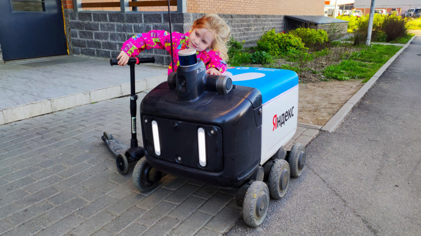 Девочка осматривает робота-курьера Яндекс у жилого дома