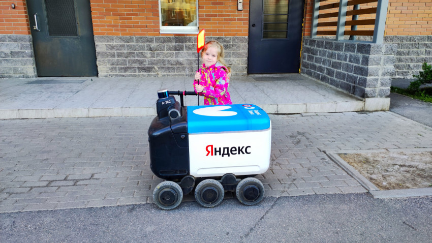 Девочка рядом с роботом-доставщиком Яндекс во дворе дома