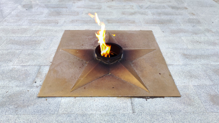 Металлическая звезда вечного огня с горящим пламенем на каменной площади в Прохладном