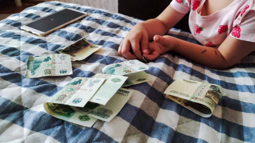 Ребёнок считает рублёвые купюры на клетчатой скатерти