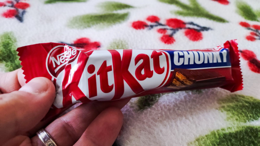 Шоколадный батончик Nestlé KitKat Chunky в руке на тканевом фоне