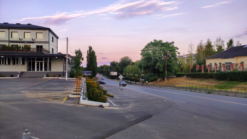 Вечерняя улица города Прохладного с дорогой, парковкой и современным зданием