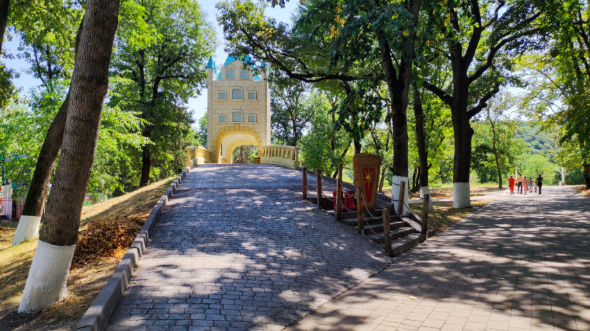 Пешеходная дорожка в Городском парке Нальчика ведёт к декоративной башне-арке среди деревьев