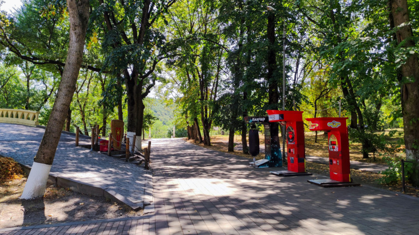 Тенистая парковая дорожка с торговыми автоматами среди деревьев