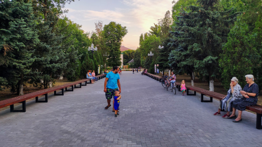 Пешеходная аллея с длинными лавочками и гуляющими людьми в парке Прохладного