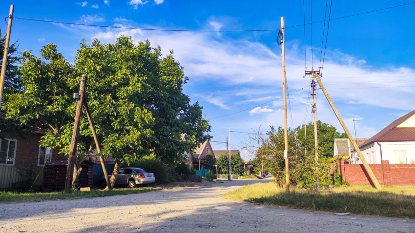 Сельская улица с грунтовой дорогой, домами и линиями электропередачи