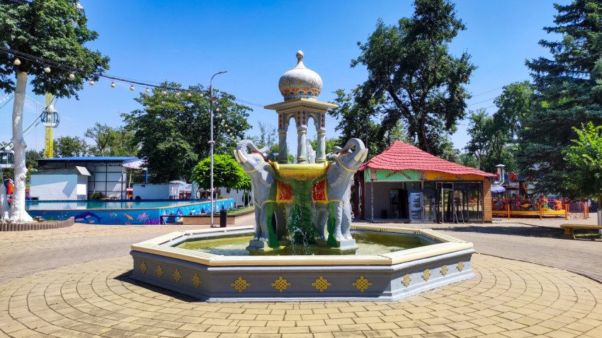 Фонтан со скульптурами слонов рядом с павильонами и аттракционами