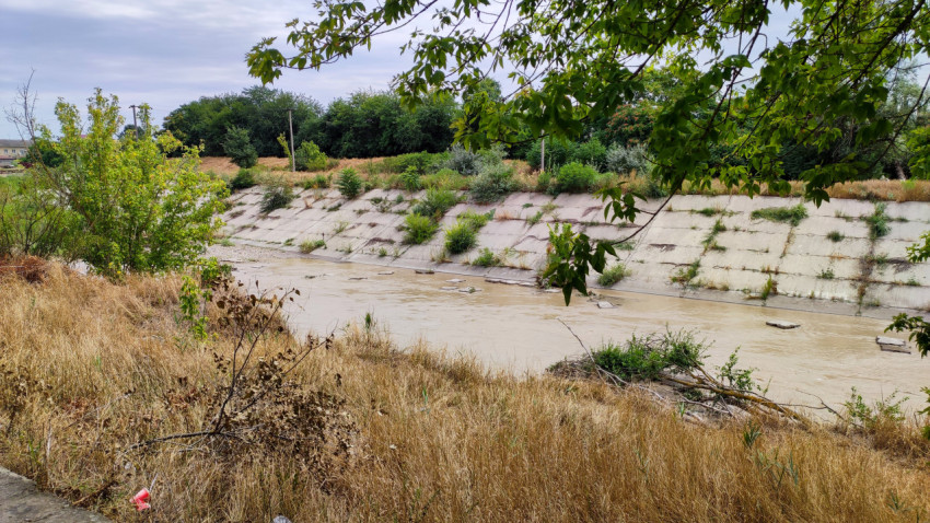Бетонированное русло реки Малка в Прохладном с мутной водой и зарослями