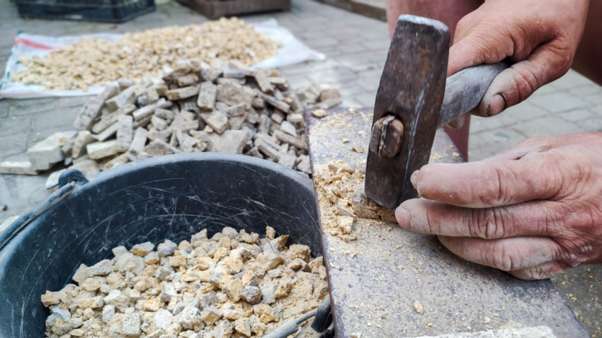 Руки с молотком дробят камень в щебень рядом с ведром