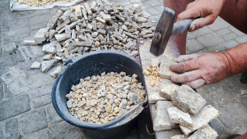 Дробление камня молотком на площадке с брусчаткой и ведром щебня