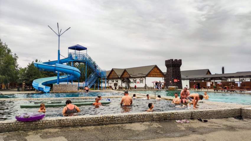 Открытый бассейн с синей водной горкой и отдыхающими на территории комплекса